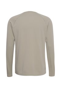 Beżowa koszula z długim rękawem z teksturowanej tkaniny z okrągłym dekoltem i subtelnym logo blisko dolnego brzegu, pokazana od tyłu.