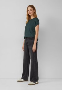 Groene geribbelde top met korte mouwen, gecombineerd met hooggewaisted donkergrijze wijde jeans en beige sneakers met zwarte strepen. Gladde texturen zichtbaar.