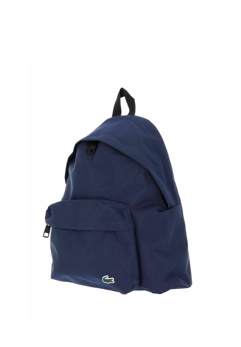 Navy blue backpack with front zippered pocket and black fabric loop handle, displaying a small green and red crocodile logo.