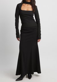Schwarzes Langarmoberteil mit quadratischem Ausschnitt, kombiniert mit einem figurbetonten schwarzen Maxirock. Glattes Material und eine elegante Silhouette.