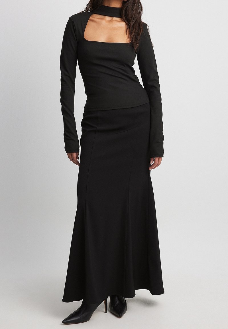 Schwarzes Langarmoberteil mit quadratischem Ausschnitt, kombiniert mit einem figurbetonten schwarzen Maxirock. Glattes Material und eine elegante Silhouette.