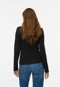 Zwarte long sleeve top gemaakt van rekbaar materiaal, getailleerd ontwerp, met een ronde halslijn. Gecombineerd met blauwe high-waisted denim jeans.