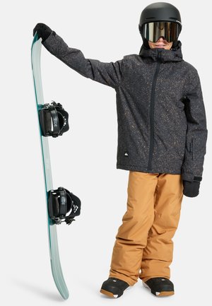 Planche à neige avec une base bleu clair et des fixations noires, tenue par une personne portant une veste noire à motifs, un pantalon orange et des gants noirs.