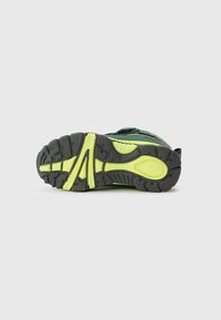 Zielona podeszwa sportowego buta z teksturowaną czarną gumową podstawą z żółtymi akcentami, zaprojektowana dla przyczepności i trwałości.