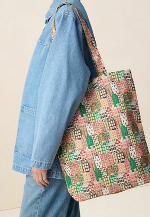 Person trägt eine hellblaue Jeansjacke und Jeans und trägt eine Tragetasche mit einem bunten Stadtbildmuster über der Schulter.