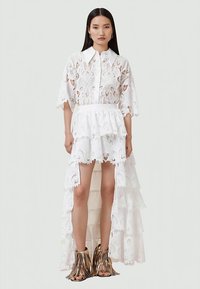 White lace dress with a collared design, short sleeves, layered skirt, and side slits; features intricate floral patterns.