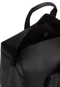 Μαύρο σακίδιο από υφασμένο νάιλον με λεία δερμάτινη βάση· διαθέτει άνοιγμα με φερμουάρ και εσωτερική ετικέτα με επωνυμία.