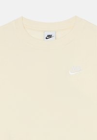 Krém színű Nike póló, környakú kivitelben, puha tapintású, a bal mellrészen kis fehér Nike logóval hímzett.