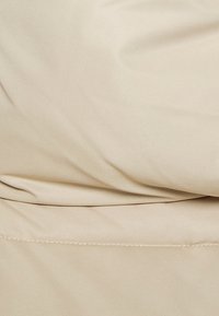 Beżowy materiał o gładkiej teksturze, z łagodnymi fałdami i subtelnym połyskiem. Brak wyraźnych wzorów lub elementów metalowych.