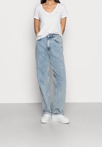 Jeans de tiro alto de color azul claro con un ajuste relajado, textura desvanecida, bolsillos laterales y dobladillos cosidos, combinados con una camiseta blanca de cuello en v.