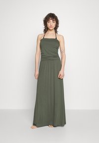 Olivově zelené maxi šaty s přiléhavým živůtkem a volnou sukní. Mají tenké ramínka a design se shromážděným páskem. Hladká, jemná textilie.