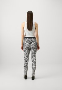 Leggins z zebrovim vzorcem v črni in beli barvi, z oprijetim krojem in elastičnim pasom, v kombinaciji z belim topom.