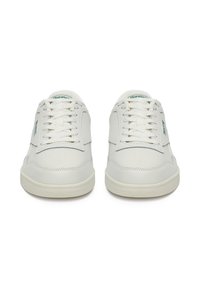 Białe sneakersy z gładką skórzaną cholewką i perforowanymi palcami dla lepszej wentylacji. Posiadają płaskie sznurówki i subtelne logo w zielonych akcentach.