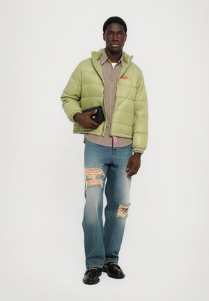 Lichtgroene pufferjack, geruite blouse, versleten blauwe jeans en zwarte schoenen, met een kleine zwarte clutch in één hand.