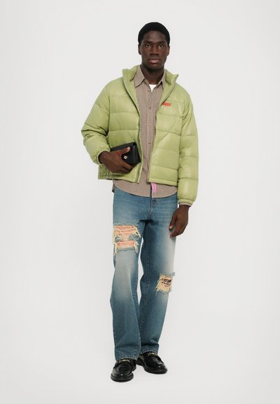 Lys grøn pufferjakke, ternet skjorte, slidte blå jeans og sorte sko, med en lille sort clutch i den ene hånd.