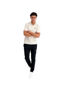 Camisa polo beige con cuello y mangas cortas, combinada con pantalones jogger negros y zapatillas blancas. Logo en la camisa y en los pantalones.