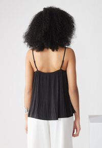 Camisola nera plissettata con spalline sottili regolabili, caratterizzata da una vestibilità fluida e una texture liscia, abbinata a pantaloni bianchi a gamba larga.
