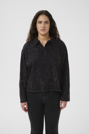 Black long-sleeve polo shirt with a textured finish, collared neck, three-button closure, and a relaxed fit. Worn with dark jeans.