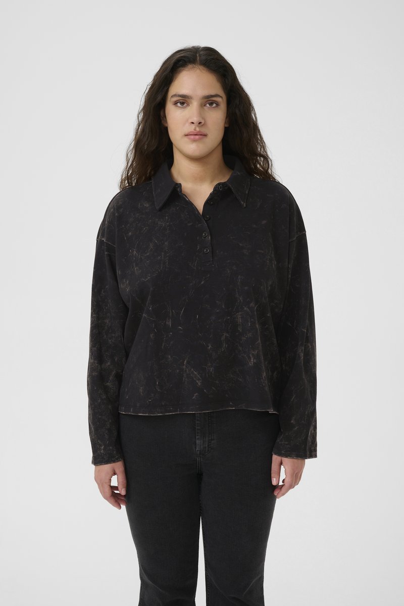 Svart langermet polo-skjorte med teksturert overflate, krage, tre knappelukking og en avslappet passform. Brukt med mørke jeans.