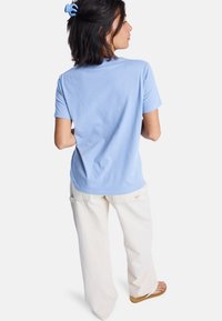 Světle modré bavlněné tričko s klasickým střihem, spárované s krémovými širokými kalhotami. Jednoduchý design, krátké rukávy a měkká textura.