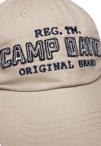 Cappellino da baseball beige in cotone con il testo ricamato "CAMP DAVID" in blu scuro e bianco, dotato di visiera curva e dettagli di cucitura.