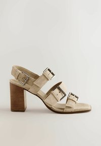 Sandale en daim beige avec trois brides réglables à boucle argentée et un talon épais en bois empilé.