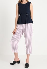 Námořnická peplum blůza s dekoračními knoflíky v pase, spárovaná s růžovými a bílými kalhotami s kostkovaným vzorem, které mají třepené lemy. Černé muly.