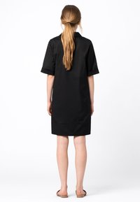 Vestito nero al ginocchio con maniche corte, vestibilità comoda e texture liscia. La parte posteriore presenta un colletto discreto e un orlo semplice.