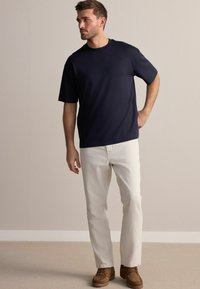 Granatowy T-shirt z krótkim rękawem zestawiony z jasnobeżowymi spodniami o prostych nogawkach oraz brązowymi butami na sznurówki. Materiał wydaje się gładki, bez wzorów.