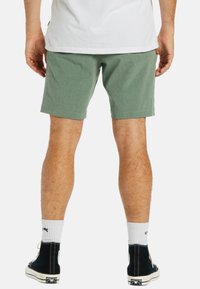 Shorts verts en tissu texturé, coupe décontractée, longueur mi-cuisse et ourlet cousu, portés avec des baskets montantes noires et des chaussettes blanches.