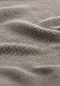 Beige, textiel met een structuur en zichtbaar ribbels en lichte golven. Materiaal lijkt zacht en buigzaam, geschikt voor verschillende toepassingen.