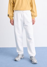 Pantalons de survêtement blancs avec une taille élastique et un cordon de serrage. Associés à un t-shirt à manches longues jaune avec un motif d'oiseau sur la manche.