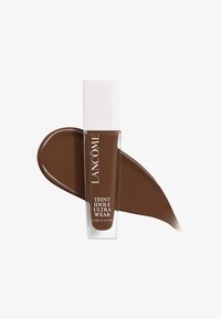 Flacon de fond de teint marron avec une base transparente et un capuchon blanc. Accompagné d'un échantillon marron lisse qui ressemble à la couleur du produit.