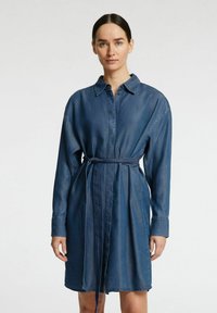 Tummansininen denimihemmetti, jossa pitkät hihat, napitettava etuosa ja yhteensopiva vyö vyötärön sääntöä varten. Pehmeä tekstuuri, rento istuvuus.