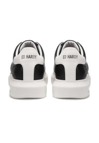 Pár černobílých tenisek Ed Hardy zobrazených zezadu, s bílými podpatky a textem "ED HARDY" a silnými bílými podrážkami.