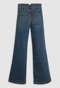 Vue arrière d'un jean en denim bleu taille haute à jambes larges avec deux poches arrière et des passants pour ceinture sur un fond uni.