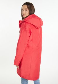 Červená nepromokavá parka s kapucí, stahovaným pasem, dlouhými rukávy a hladkým povrchem. Má rovný střih a minimální detaily z hardware.