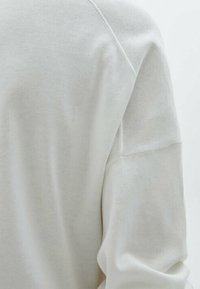 Maglione grigio chiaro in un morbido tessuto testurizzato. Presenta maniche raglan e una vestibilità rilassata, accentuata da un colletto leggermente a coste.