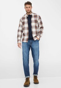 Karierter Langarmshirt in Weiß, Braun und Blau, kombiniert mit dunkelblauen Jeans und braunen Stiefeln, mit hochgeschlagenen Ärmeln.