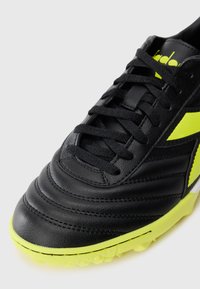 Black leather soccer shoe with neon yellow sole and logo, black laces, and textured front for turf play.