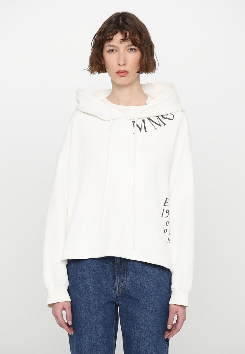 Λευκό φούτερ από βαμβάκι με κορδόνια, μπροστινές τσέπες και γραφικό κείμενο στα μανίκια και στο στήθος. Συνδυάζεται με ψηλόμεσα μπλε τζιν.