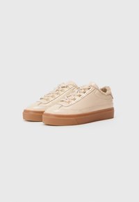 Baskets en cuir beige avec une semelle en caoutchouc texturé tan, dotées d'œillets dorés et d'un col rembourré pour un confort supplémentaire.
