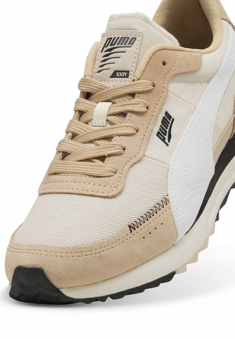 Zapatillas Puma con una parte superior de gamuza y malla en color beige, detalles en blanco, cordones redondos y una suela de goma negra texturizada.