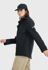 Veste noire imperméable avec fermeture éclair à l'avant et capuche, assortie d'une casquette marine. Elle présente un fit ajusté et des manches réglables pour plus de confort.