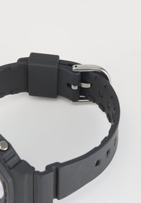Bracelet de montre en caoutchouc noir avec une surface texturée, doté d'une boucle en métal argenté et d'un passant rectangulaire pour l'ajustabilité.