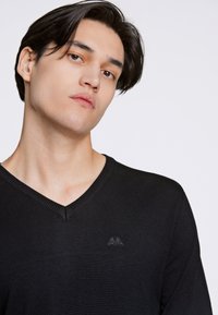 Maglione nero a V in un tessuto a maglia liscia con scollo a costine. Presenta un piccolo logo sul petto, evidenziando un design minimalista.