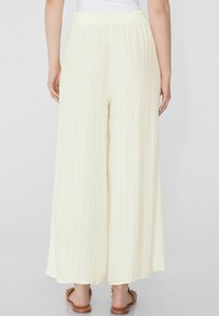 Pantalones de pierna ancha en amarillo claro con un diseño texturizado y acanalado. Cintura elástica y ajuste relajado, combinados con sandalias planas marrones.