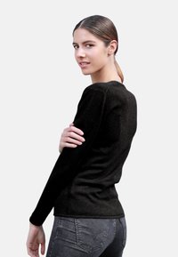 Haut noir à manches longues avec un col rond, design ajusté, texture douce et style minimaliste, associé à un jean foncé.