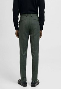 Gröna skräddarsydda byxor med slim fit, texturerad tyg och dubbla fickor, matchade med svarta skor och en mörk tröja.