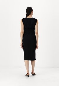 Melnas bez piedurknēm kleitas ar pieguļošu augšdaļu, smockētu jostasvietu un ceļa garuma svārkiem, kas izgatavota no gludas auduma. Nēsāta kopā ar melnām augstpapēžu sandālēm.